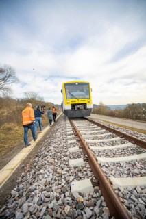 A train on rails with photographers in orange vests in a natural environment, acceptance of the