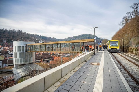 A train approaches a station with a wide panorama and hills in the background, taking off the