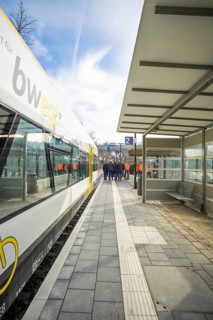 A train station with a stopping train and a group of people moving on the platform, acceptance of