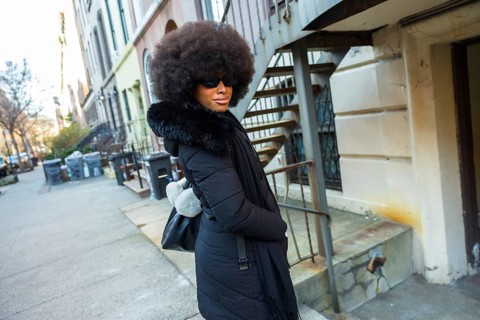 Young woman with big afro hairstyle wearing sunglasses and a fashionable black winter coat with fur
