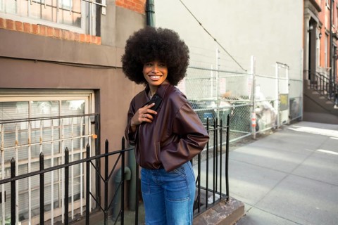 Young african american woman with a large afro hairstyle smiling, wearing a leather jacket and