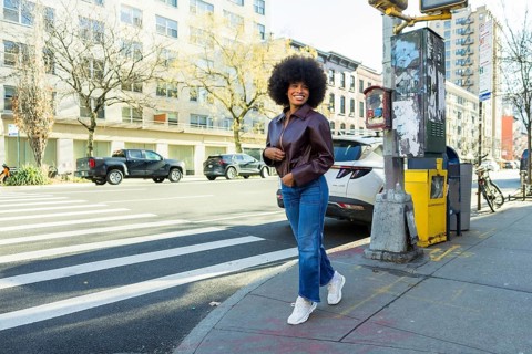 Young black woman smiling confidently, walking briskly on a manhattan city street, wearing a