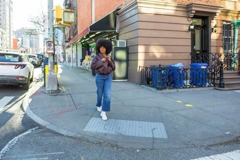 Young woman with natural afro hair walking confidently along a residential brownstone building on a