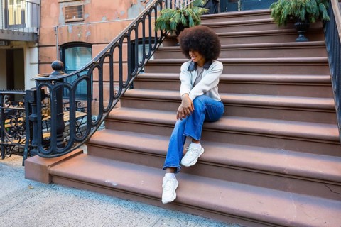 Young african american woman with an afro hairstyle sitting casually on brownstone stoop steps.
