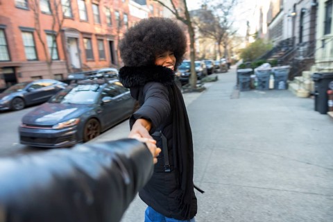 Smiling young african american woman in a winter coat leading a journey, holding hands with a