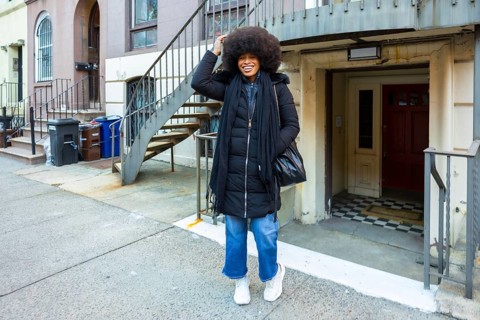 Joyful black woman with afro smiling confidently on a manhattan brownstone street in casual winter