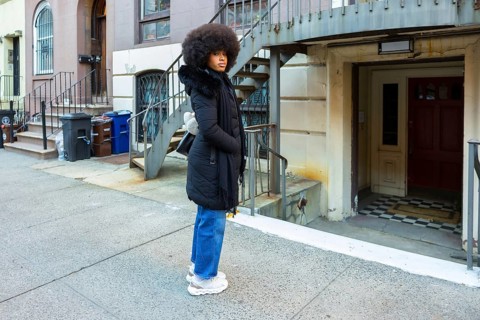 Young woman with large afro hair wearing a black winter coat and blue jeans standing on a city