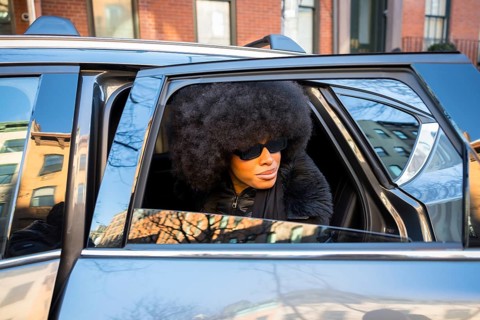 Elegant black woman wearing large sunglasses and an afro hairstyle, looking out of a car window