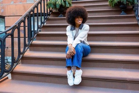 Young black woman sitting on brownstone steps in harlem, smiling and relaxed in casual street