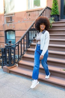 Smiling woman with afro hair descending brownstone steps in new york city, expressing joy and