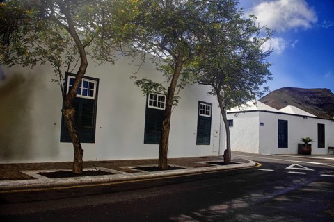 White building with green shutters and trees along the road, Yaiza Lanzarote