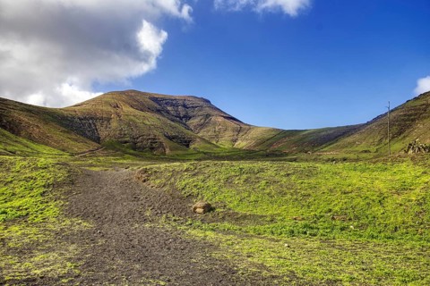Trail leads through green hills under a sunny sky, Yaiza Lanzarote