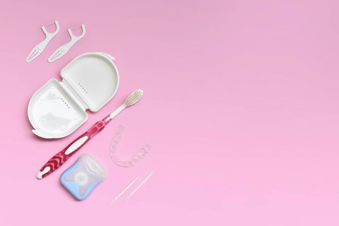 Top view of dental clear aligners, toothbrush, toothpicks and floss on pink background with copy