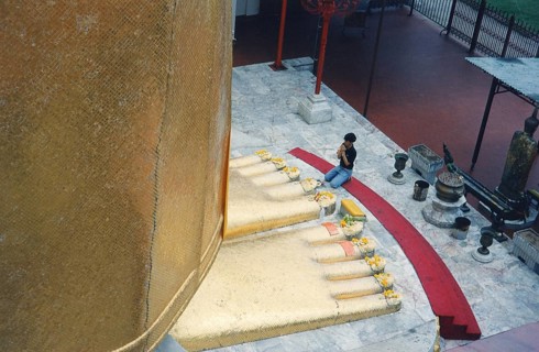 The huge golden Buddha at Wat Indravihan. A Buddhist prays at the feet of the big standing Buddha.