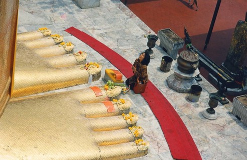 The huge golden Buddha at Wat Indravihan. A Buddhist woman prays at the feet of the big standing