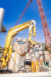 Large yellow excavator on a construction site surrounded by construction cranes, carpentry, new