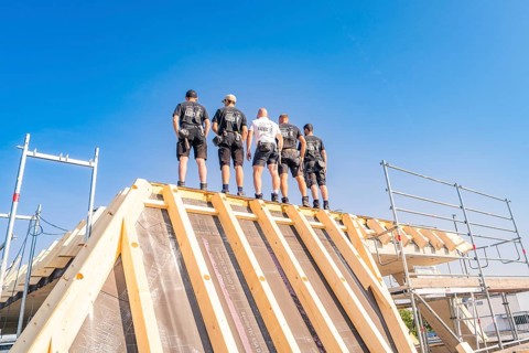 A group of construction workers standing on a roof structure under a blue sky, carpentry, new