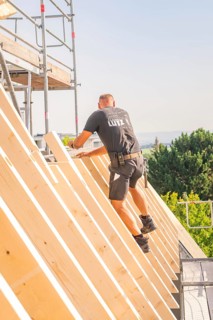 A construction worker climbs up a wooden structure on scaffolding against a blue sky, carpentry,
