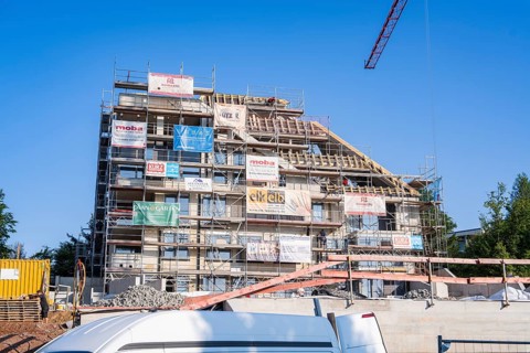 Multi-storey building with scaffolding and banners under clear, sunny sky, carpentry, new building,
