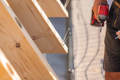 Worker holding drill next to wooden board with screws already screwed in, carpentry, new building,