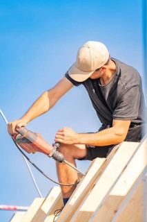 Construction worker working with a drill on a roof in sunny weather, carpentry, new building,