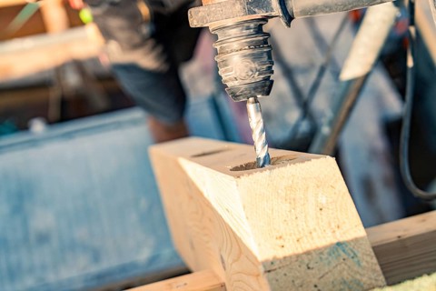 Detailed view of a drill drilling a hole in wood on a construction site, carpentry, new building,