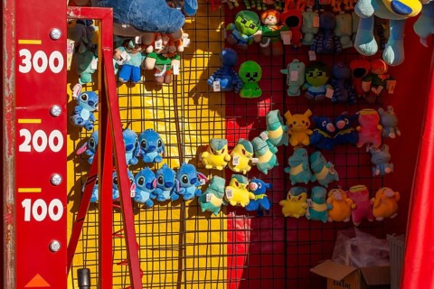 Close-up of blue, yellow and green plush prize dolls at game kiosk at Fun Show traveling ride park,