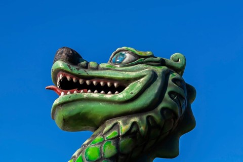 Green dragon with big teeth and long red tongue against blue sky background, Fun Show traveling