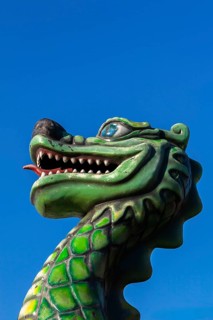 Green dragon with big teeth and long red tongue against blue sky background, Fun Show traveling