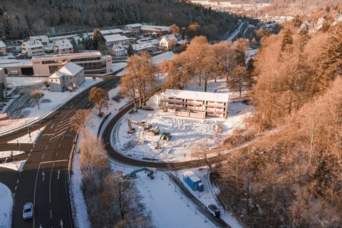 Snow-covered construction site and roads with a view of a wintry settlement and forest, Nagold,