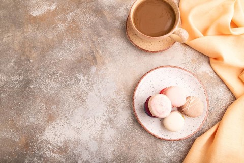 Macarons colourful cookies dessert, cup of coffee, on brown concrete background with orange linen