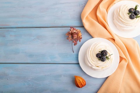 Pavlova Meringue dessert with crisp meringue and blueberry on blue wooden background with orange