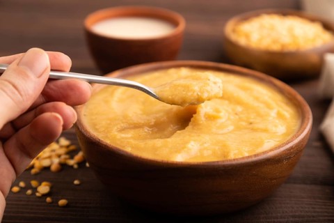 Pea cream soup, Puree, porridge in wooden bowl with hand on wooden background and linen textile.