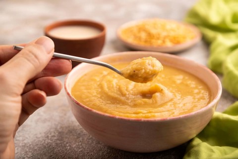 Pea cream soup, Puree, porridge in ceramic bowl with hand on brown concrete background and green