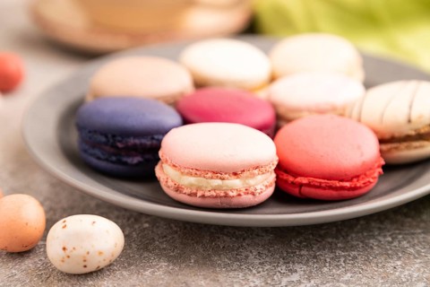 Macarons colourful cookies dessert, cup of coffee, on brown concrete background with green linen