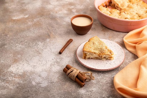 Apple Charlotte cake on brown concrete background and orange linen textile, cup of milk, side view,