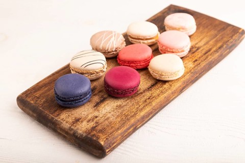 Macarons colourful cookies dessert on brown wooden cutting board on white wooden background, close