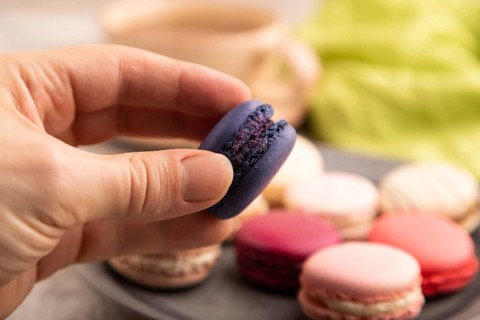 Macarons colourful cookies dessert with hand on brown concrete background with green linen textile,