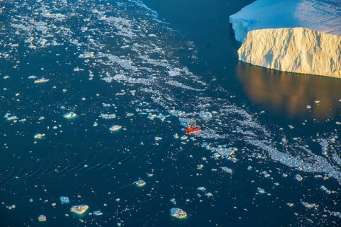 Aerial view of a tourist ship navigating through the fjord among icebergs calved from the