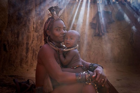 Ovahimba or Himba woman with a baby inside traditional hut, Kaokoland, Kunene Region, Namibia