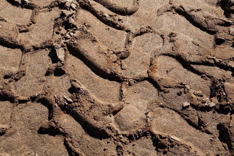 Close-up and top view of deep tire tracks made by earth loader in light brown sand at construction