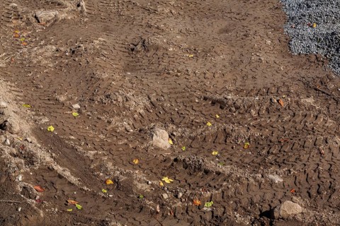 Deep tire tracks made by earth loader in light brown wet sand at construction site in early autumn,