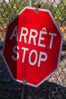 Close-up of bright red bilingual French arret and English stop sign with wire mesh fence in