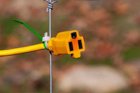 Close-up of yellow female rubber connector power plug attached to wire mesh fence with plastic tie