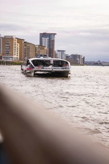 A boat on a wide river with modern buildings in the background and a cloudy sky, London, England,