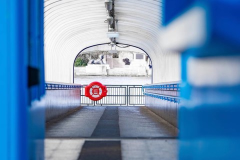 A modern passageway leads to a river, accented with a blue lifebuoy, London, England, Great Britain