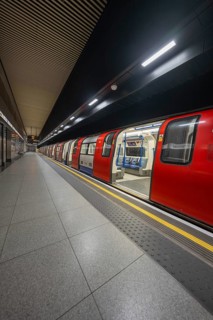 An incoming red subway train stands at an illuminated platform in a dark train station, London,