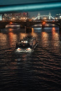 An illuminated boat on a river at night under a bright bridge in the city, London, England, Great