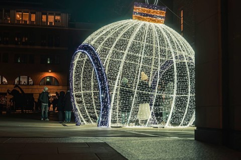 Large illuminated Christmas ball in public square with passers-by at night, London, England, Great