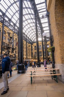 Interior with beer benches and people surrounded by vaulted brick walls and a glass roof, London,